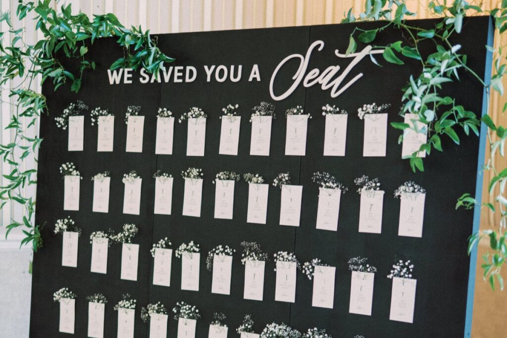 "We saved you a seat" black sign with seating chart and greenery