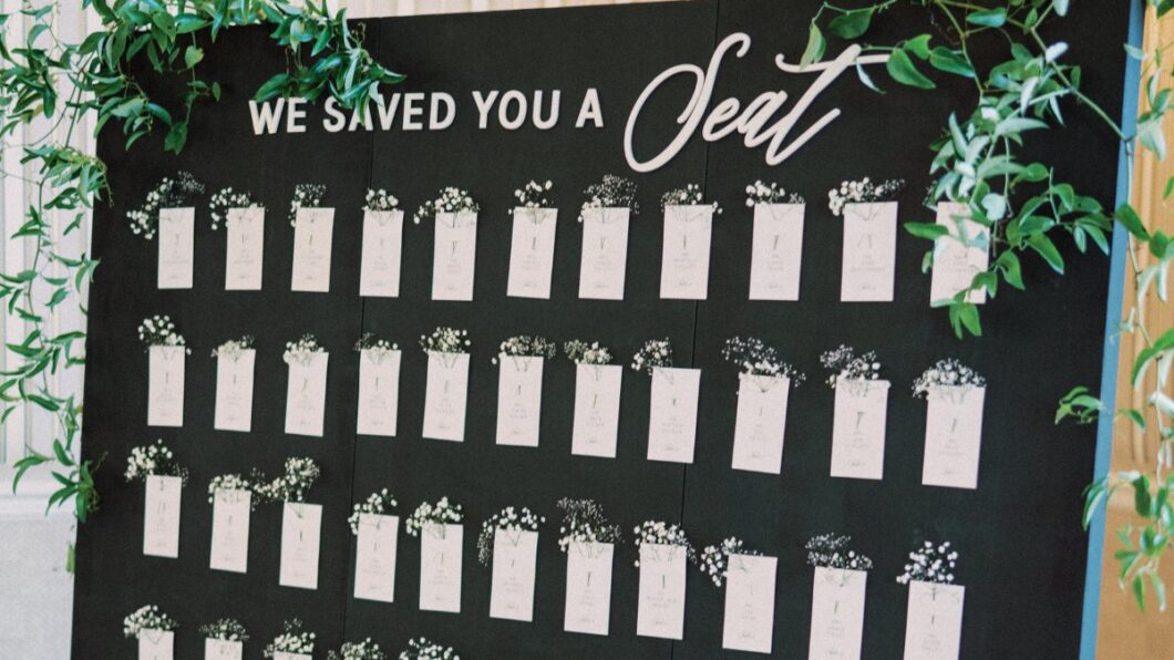 "We saved you a seat" black sign with seating chart and greenery