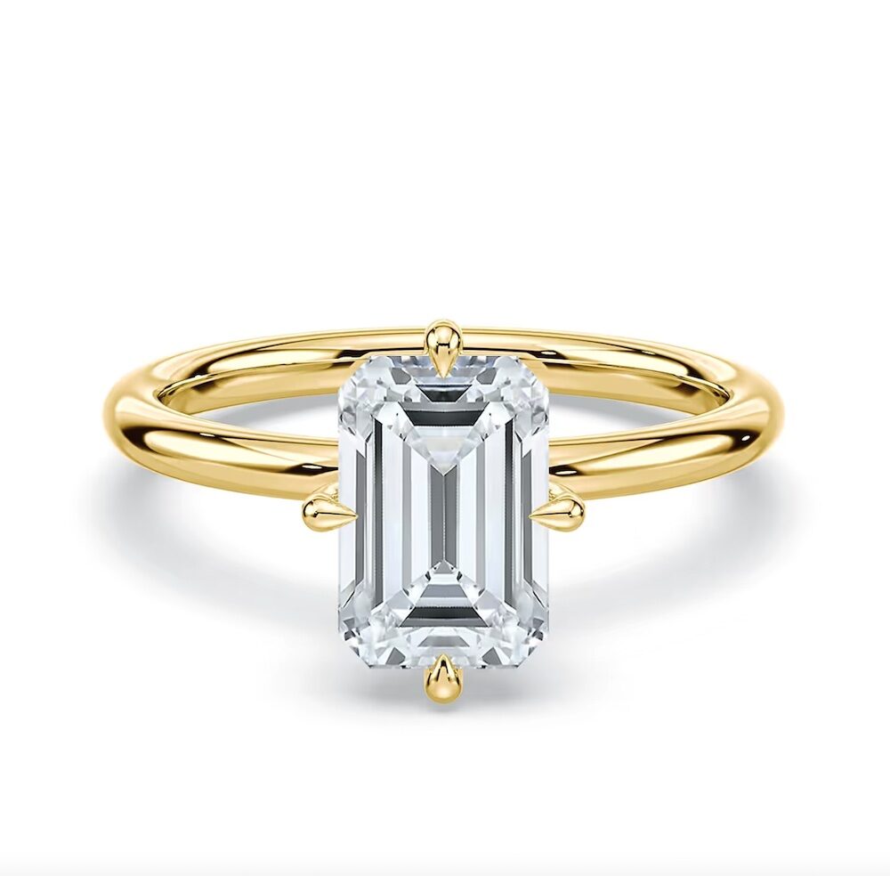 A gold band ring featuring a large, rectangular emerald-cut clear gemstone set in a simple four-prong setting.