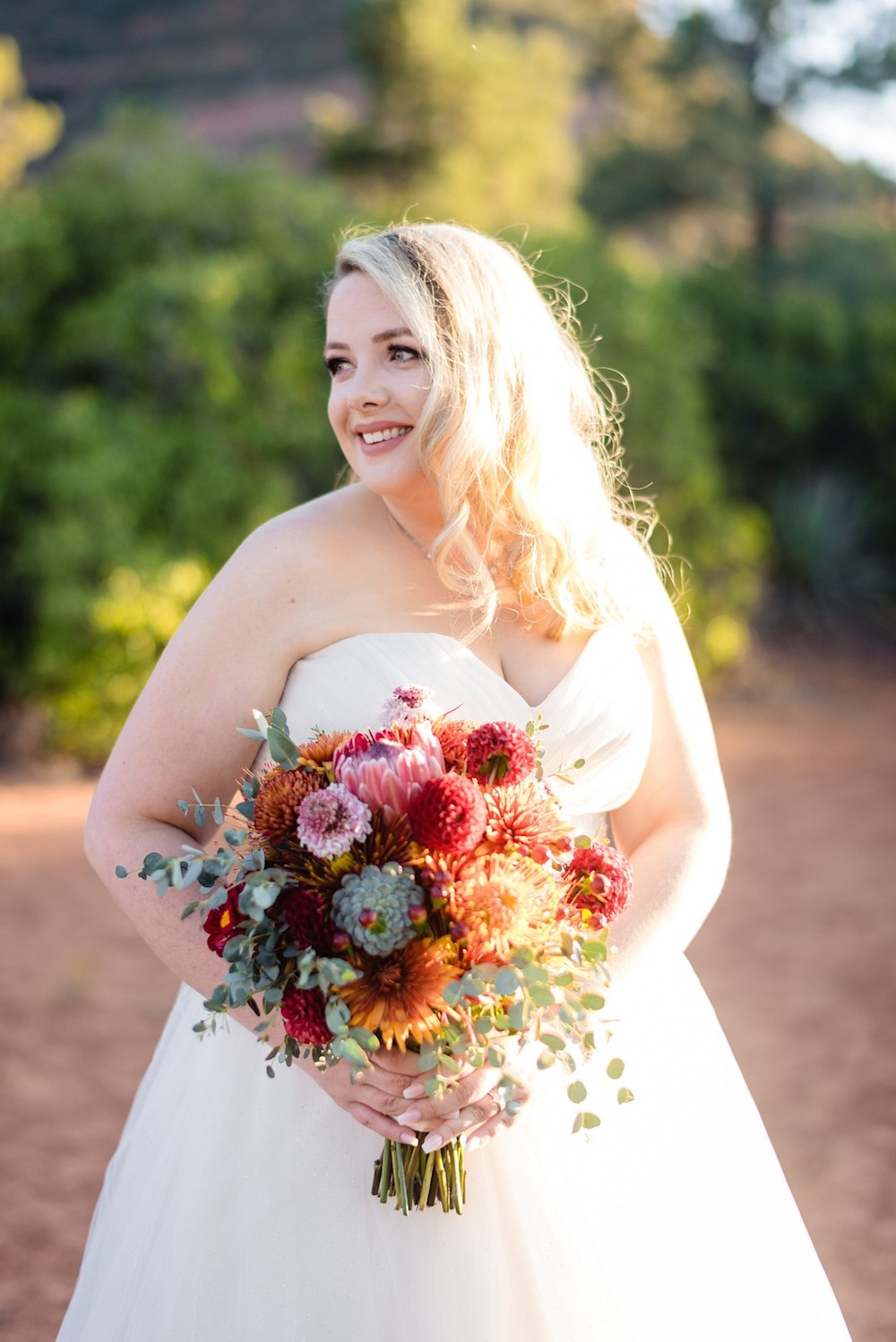 bride in red rocks of sedona holding a fall colored bouquet