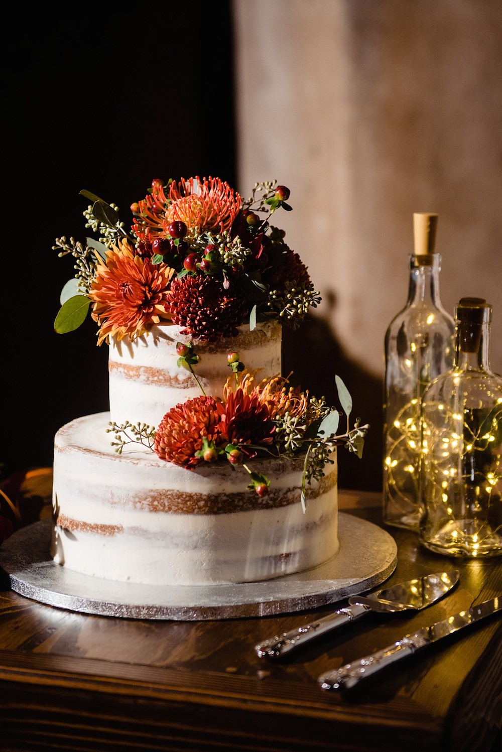 tiered wedding cake with fall colored flowers cascading down the side of it
