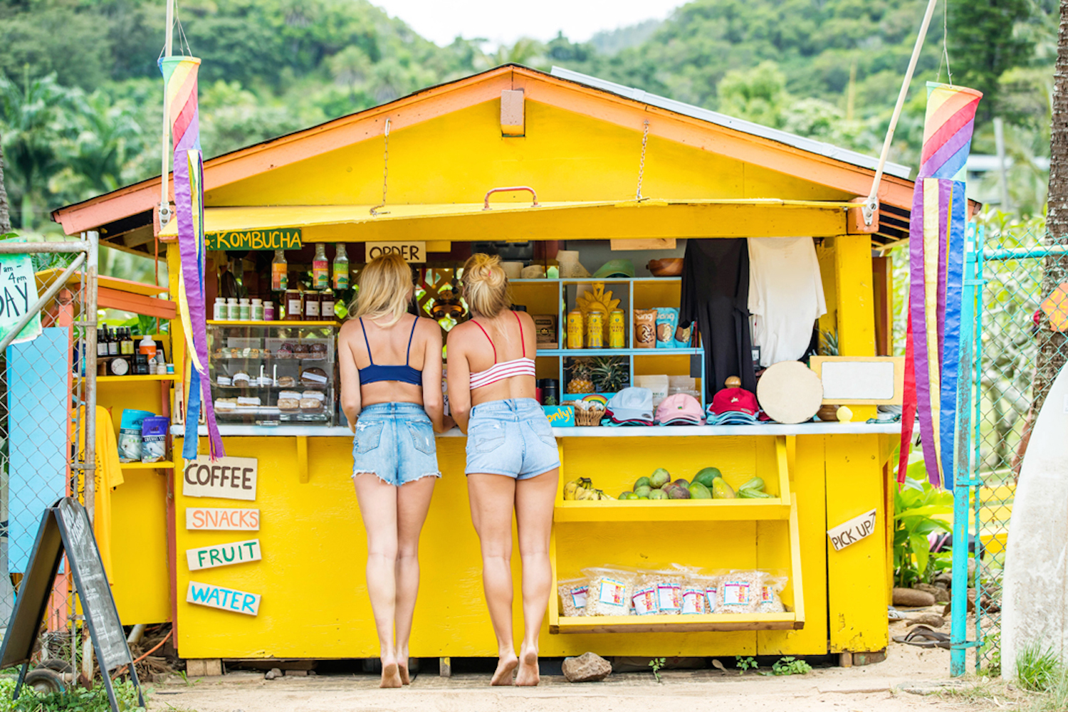 surfer girls by a bright yellow surf shack