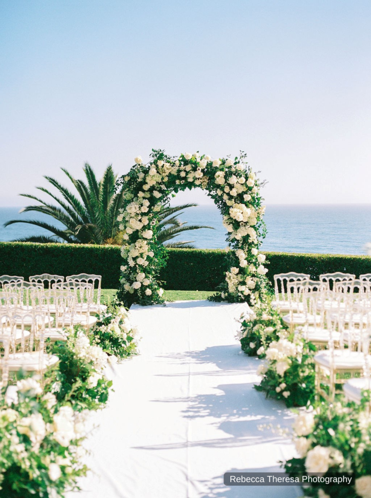 white rose arch with greenery by ocean