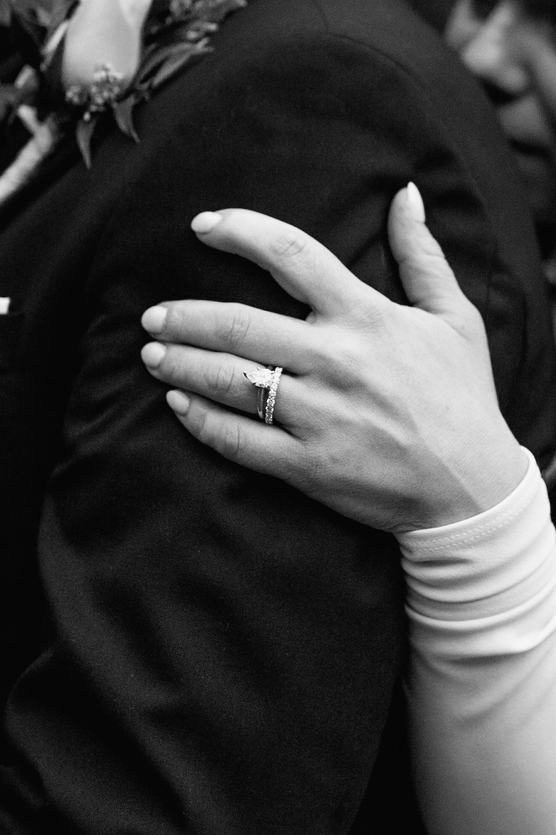 bride with long sleeve holds groom's shoulder with tear drop diamond ring