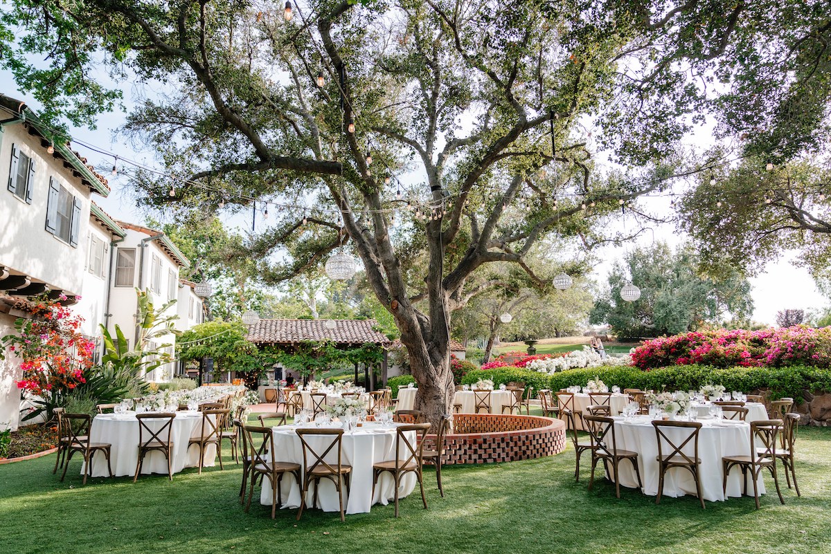 reception set up in green backyard under a oak tree next to a spanish style white home