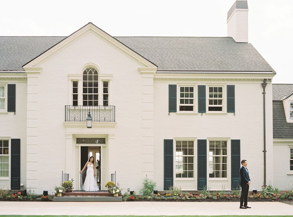 bride walks out front door of Southern vintage building with white brick