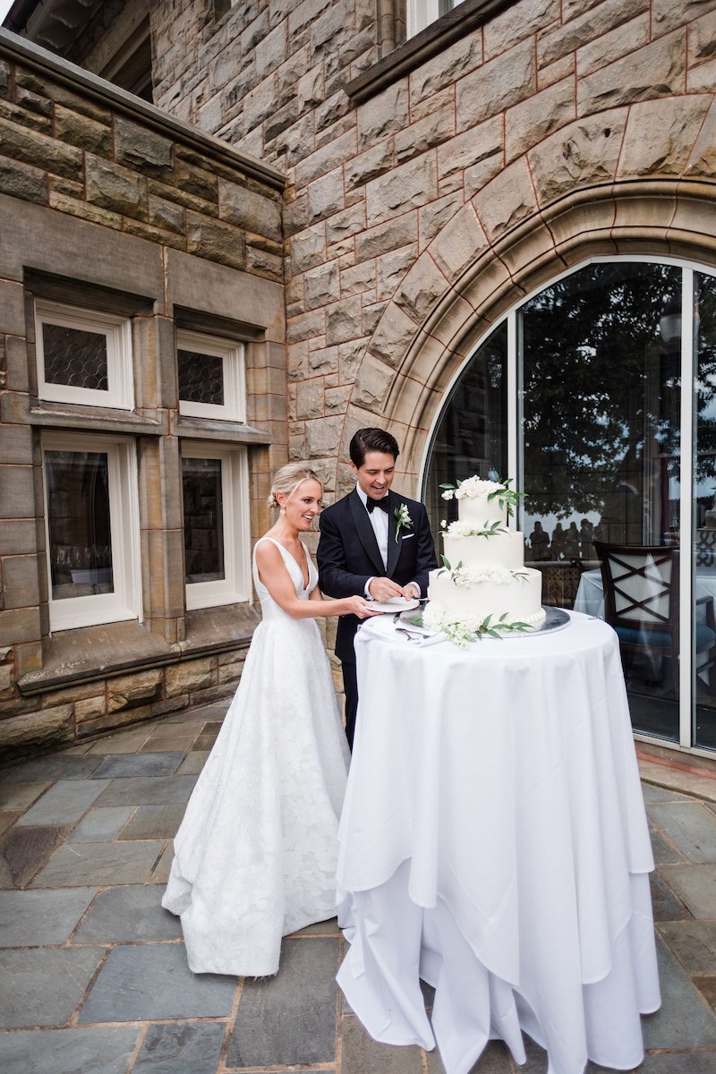 couple cutting three tier wedding cake in outdoor corner of castle building
