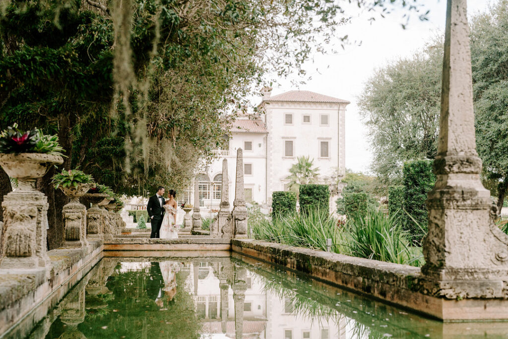 bride and groom stand looking lovingly at each other on a bridge of a European influenced wedding venue with a reflection pool