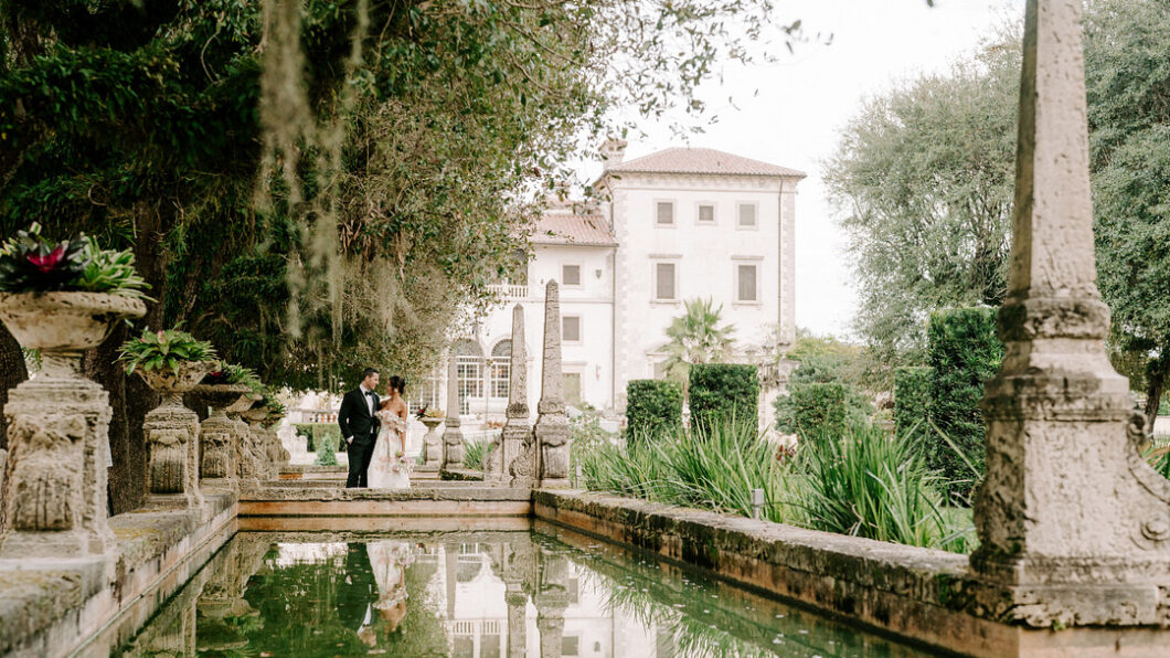 bride and groom stand looking lovingly at each other on a bridge of a European influenced wedding venue with a reflection pool