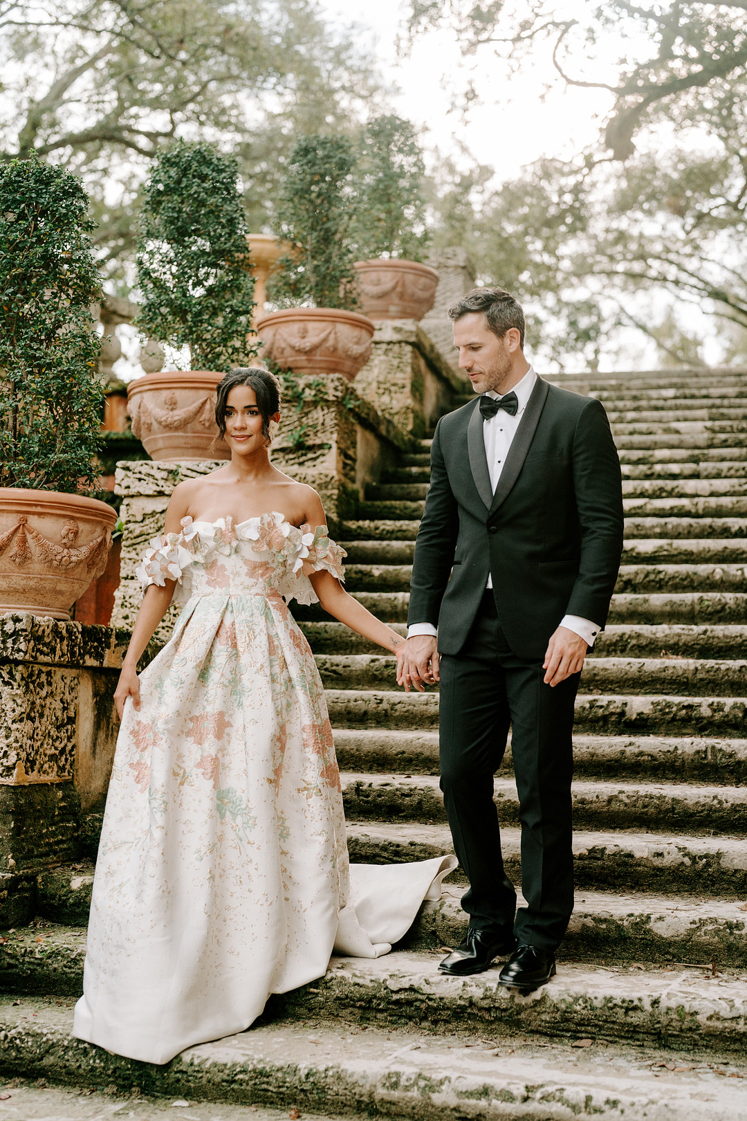 bride and groom walk down concrete steps with an old patina and potted plants framing the staircase