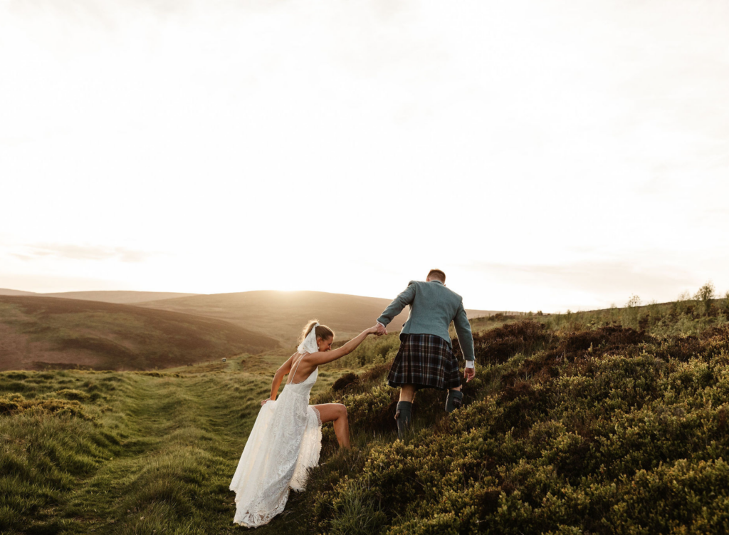 groom helps bride up hill in scottland