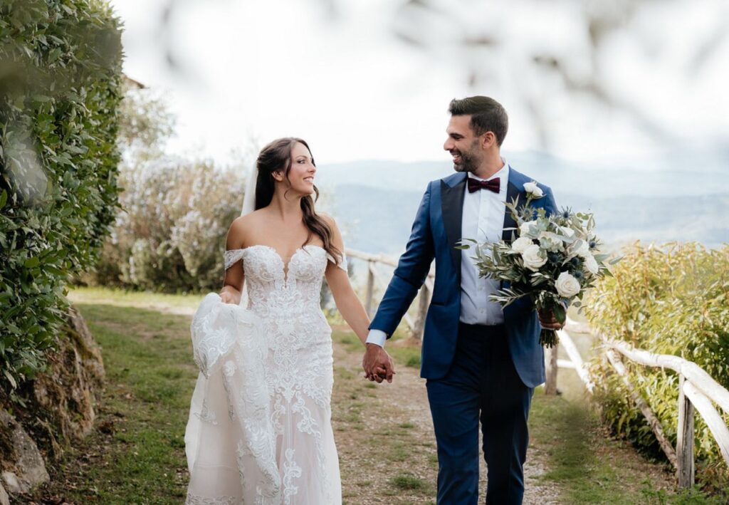 couple walk hand-in-hand with Tuscany backdrop