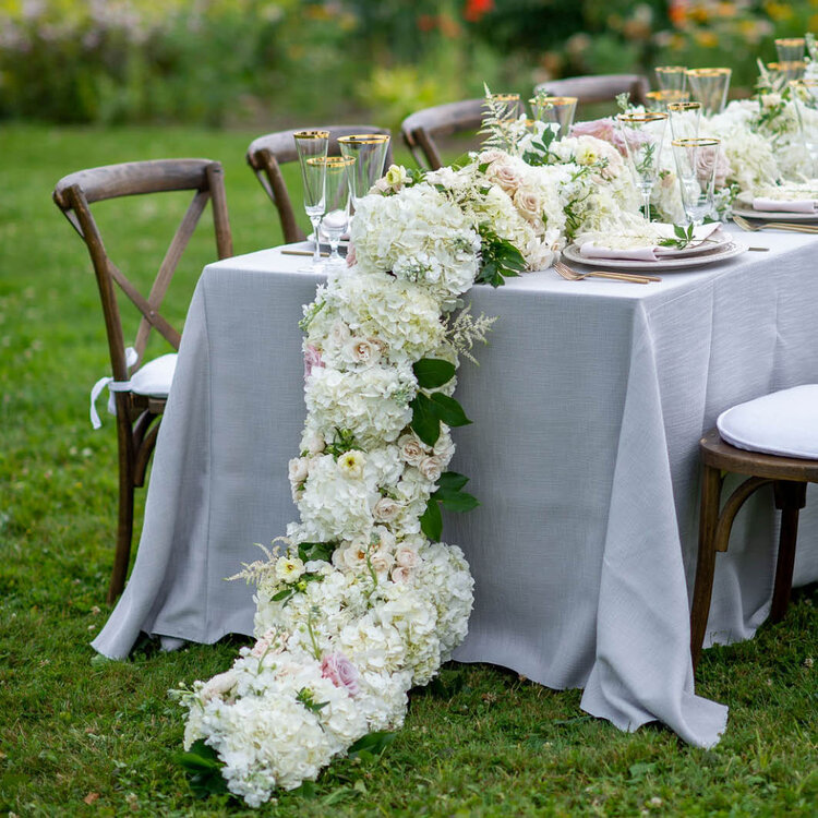 Table setting outdoors with flowery centerpiece trailing off of table
