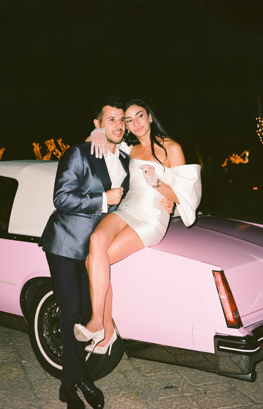 Bride and groom pose on a classic pink Cadillac
