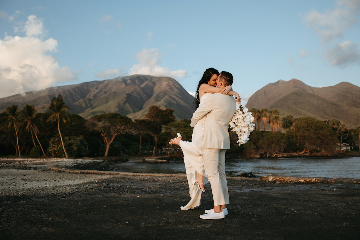 Married couple in wedding dress and suit kissing on Hawaiian beach