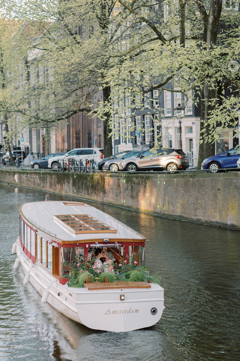 White traditional houseboat in canal in Amsterdam. Married couple kisses among flowers on the boat.