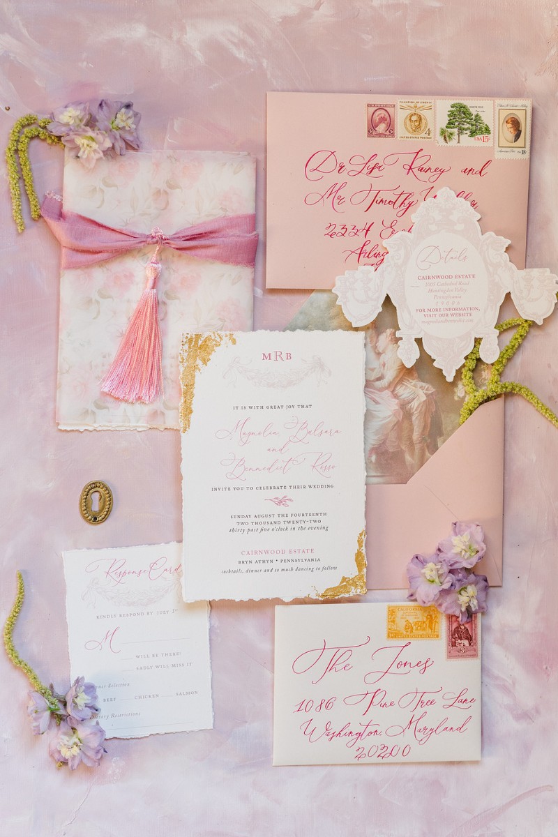 Arrangement of wedding invitation and embellishments all in different hues of pink