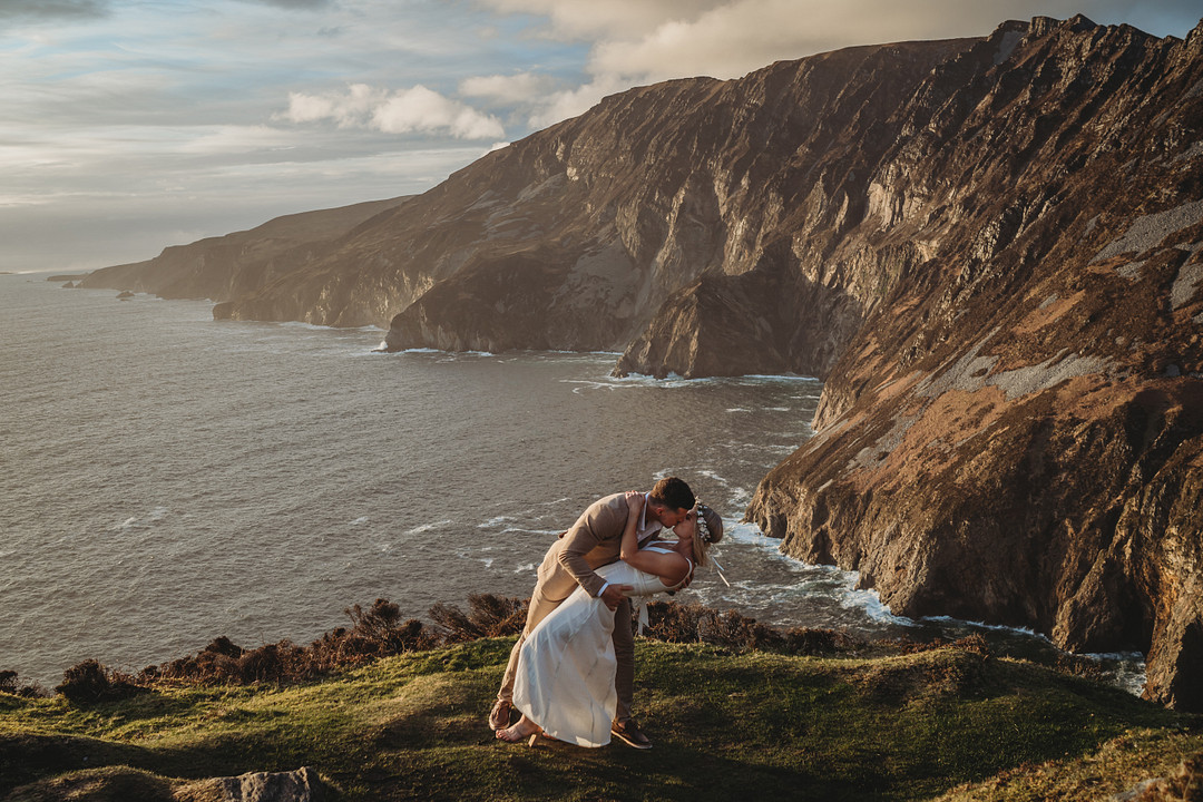 A bride and groom kiss romantically during their elopement on the cliffside in Ireland