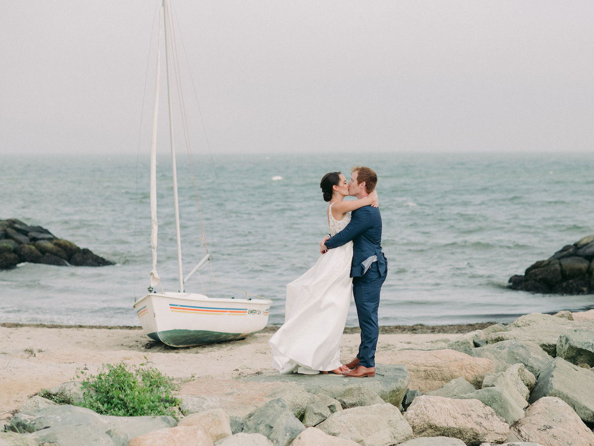 Beachside bride and groom kissing by sailboat