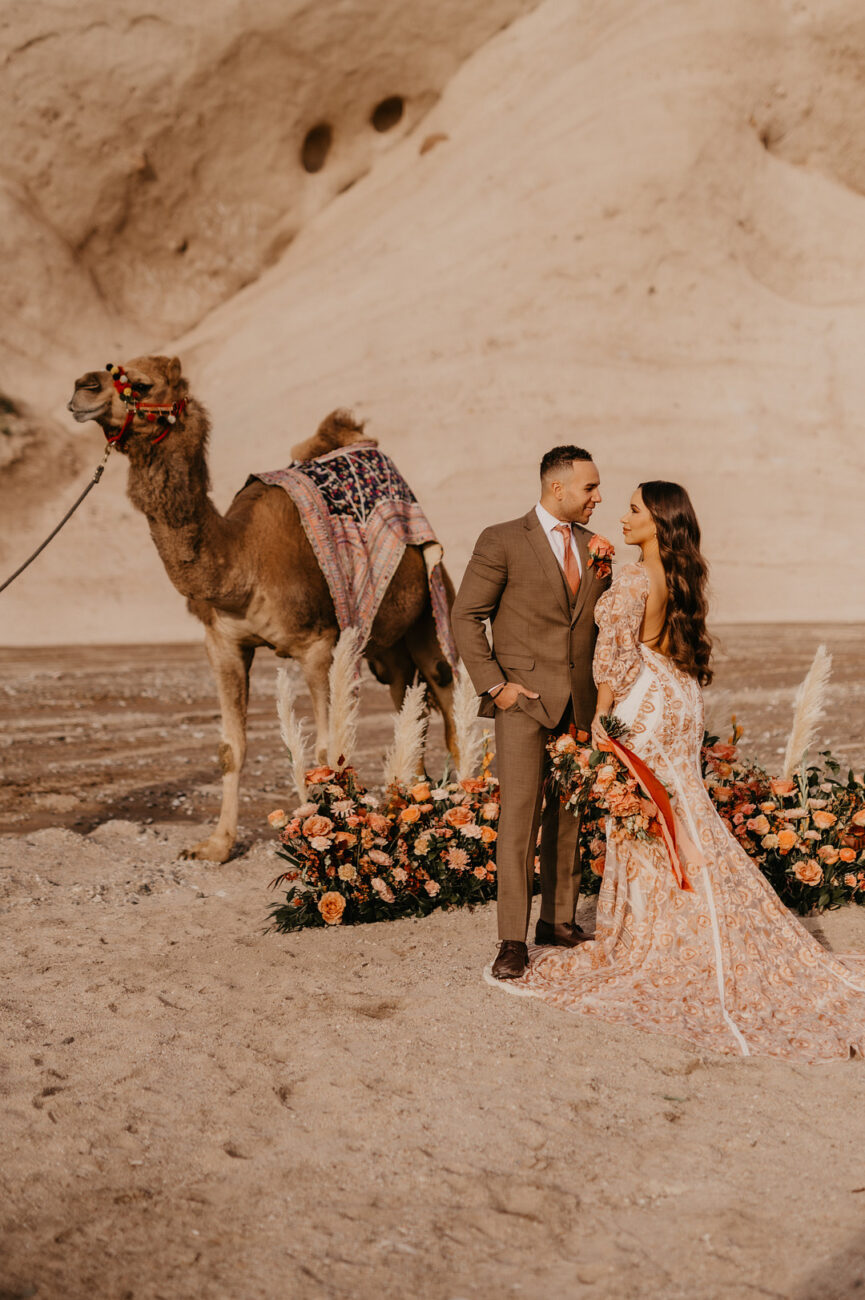 Bride and groom posing amid florals and a camel
