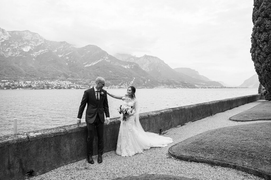 bride taps grooms shoulder for first look with Lake Como and mountains in background