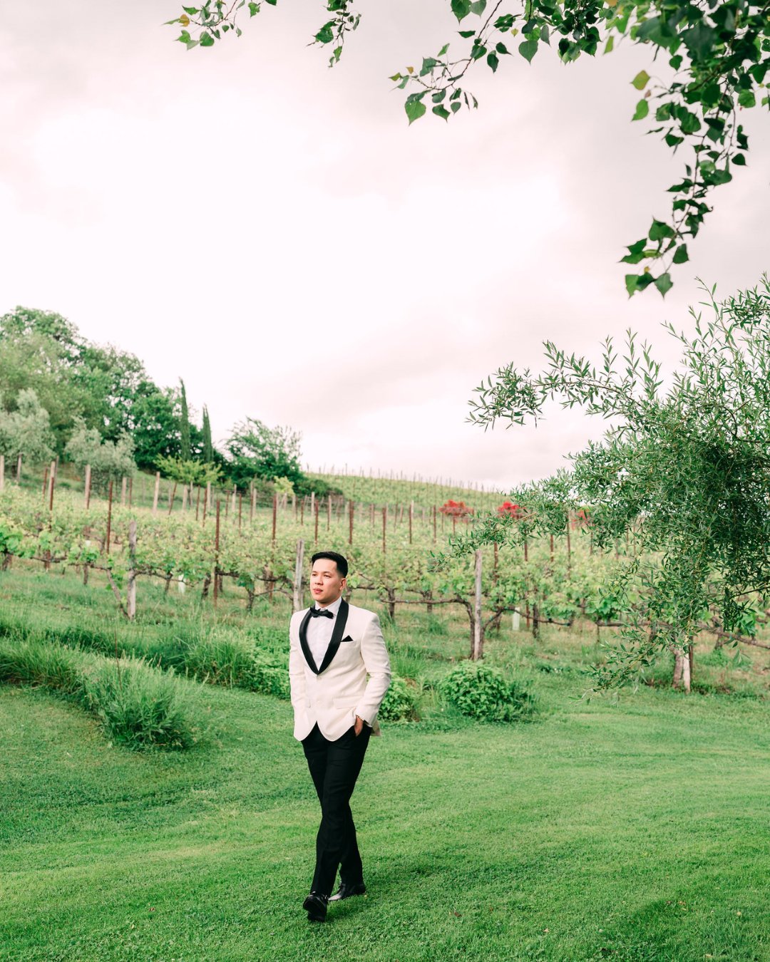 Groom strolling through vineyards in a white tux jacket and black slacks