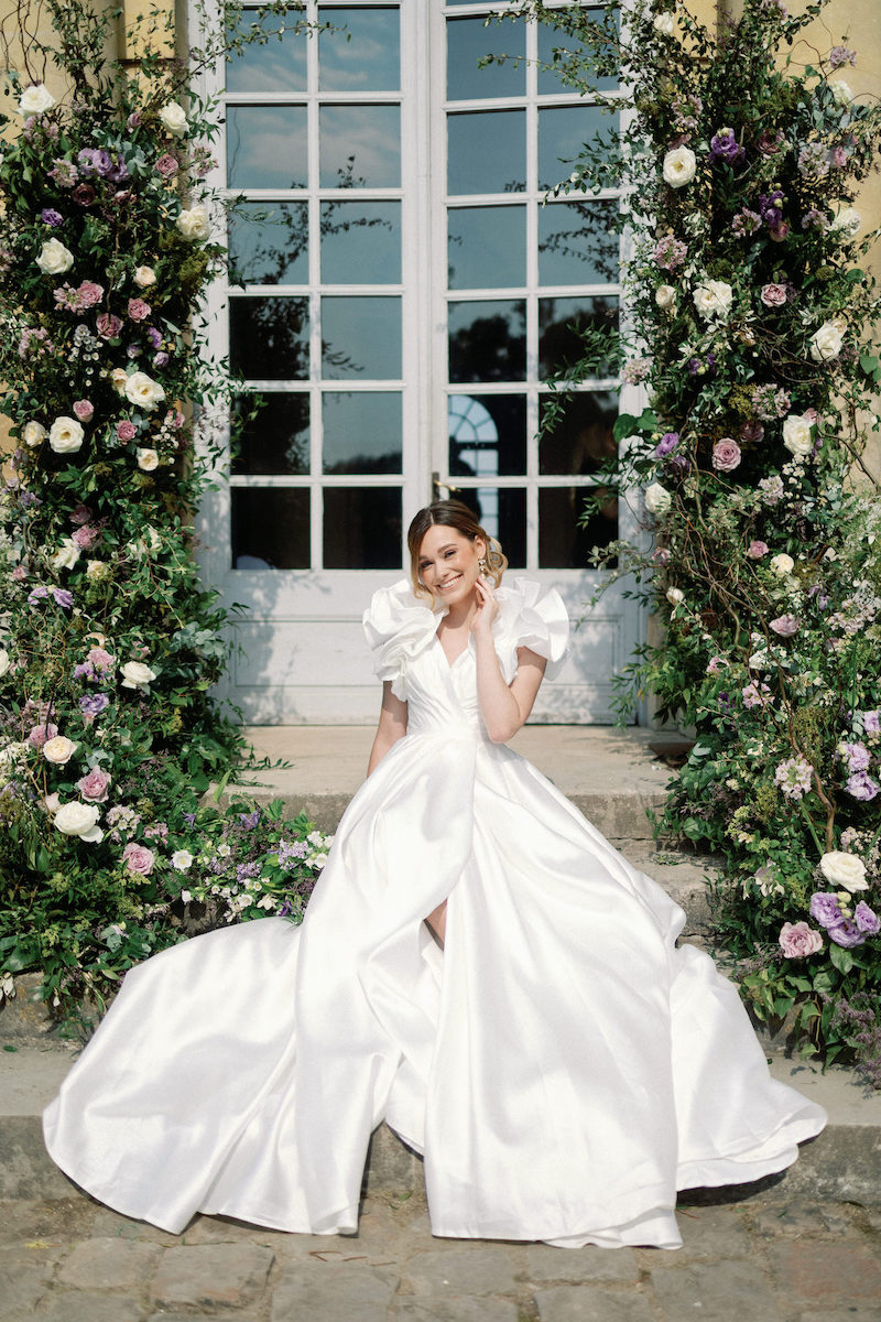 bride poses in puffy sleeved white dress in front of French doors