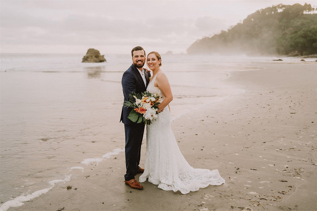 bride and groom pose on Costa Rica beach with gray sky