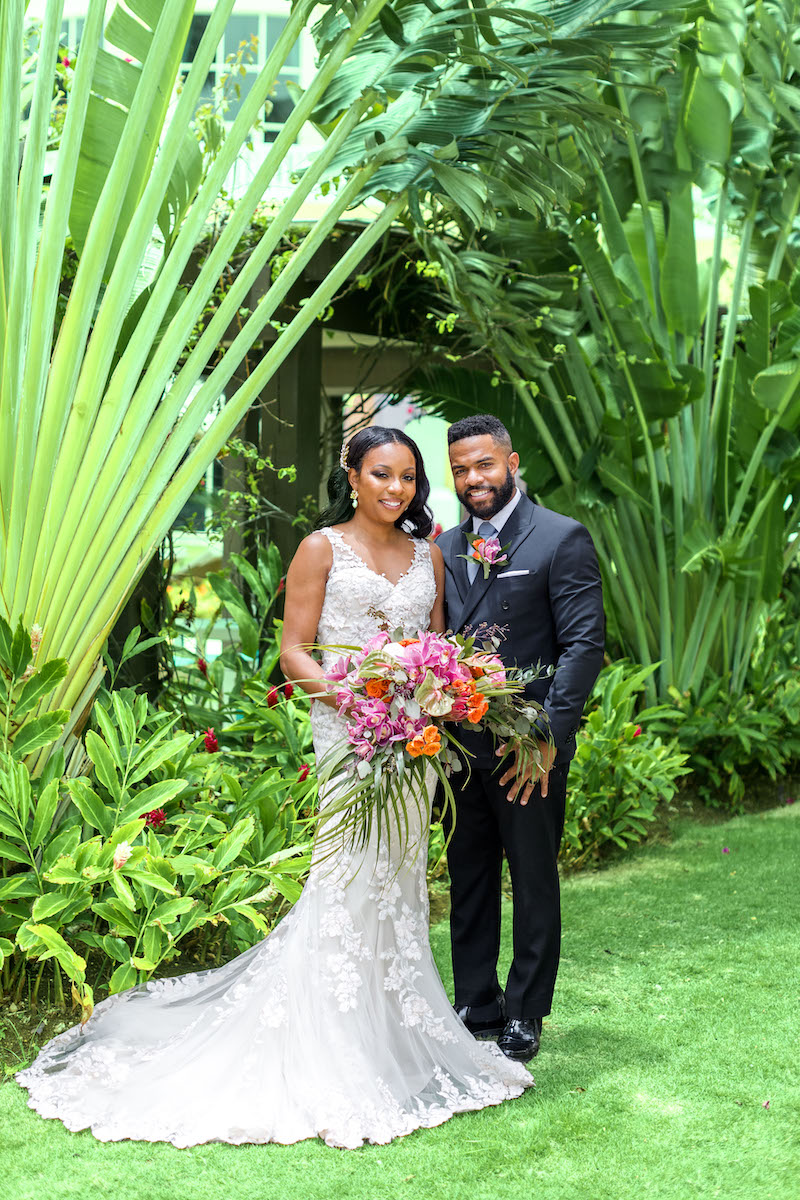 bride with pink bouquet and groom in suit around tropical plants