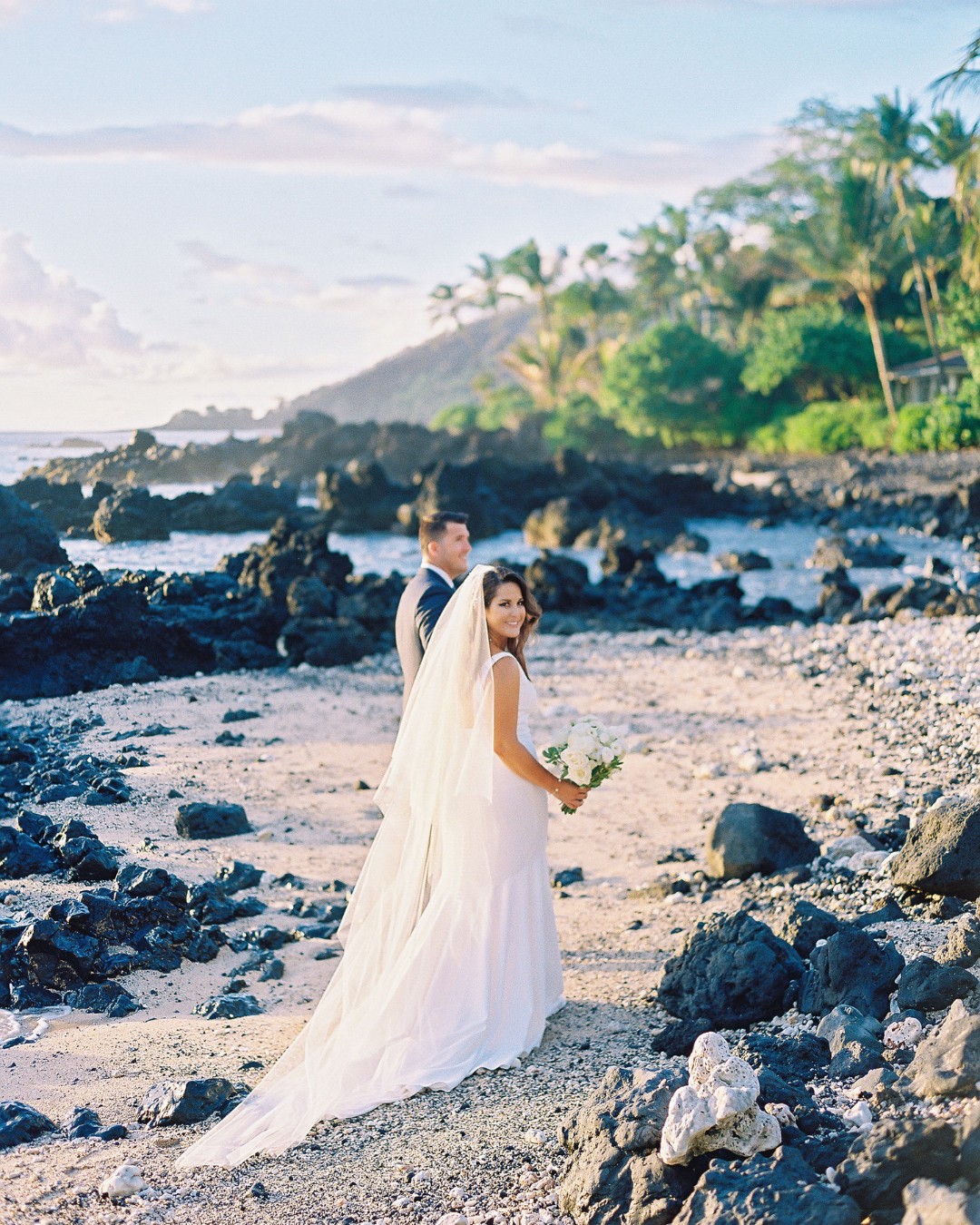 bride and groom walk along rocky beach