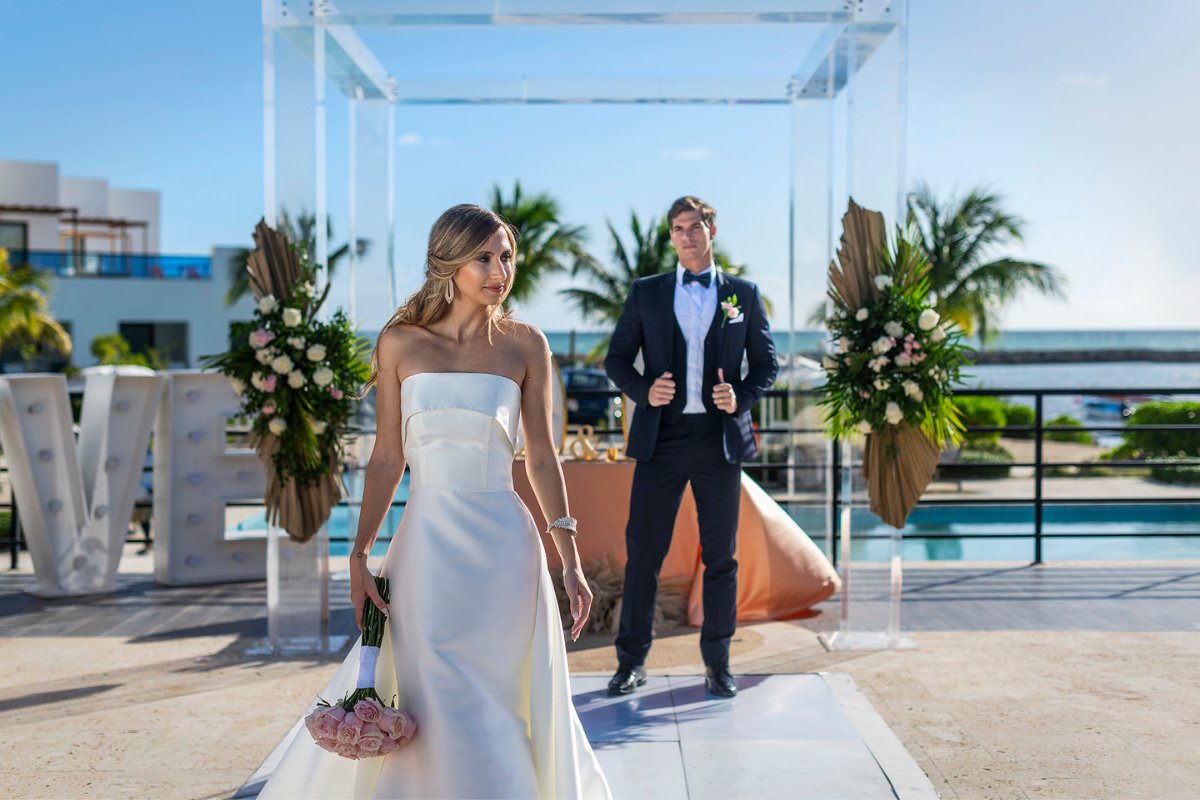 bride stands in front of groom at altar with palms in the back