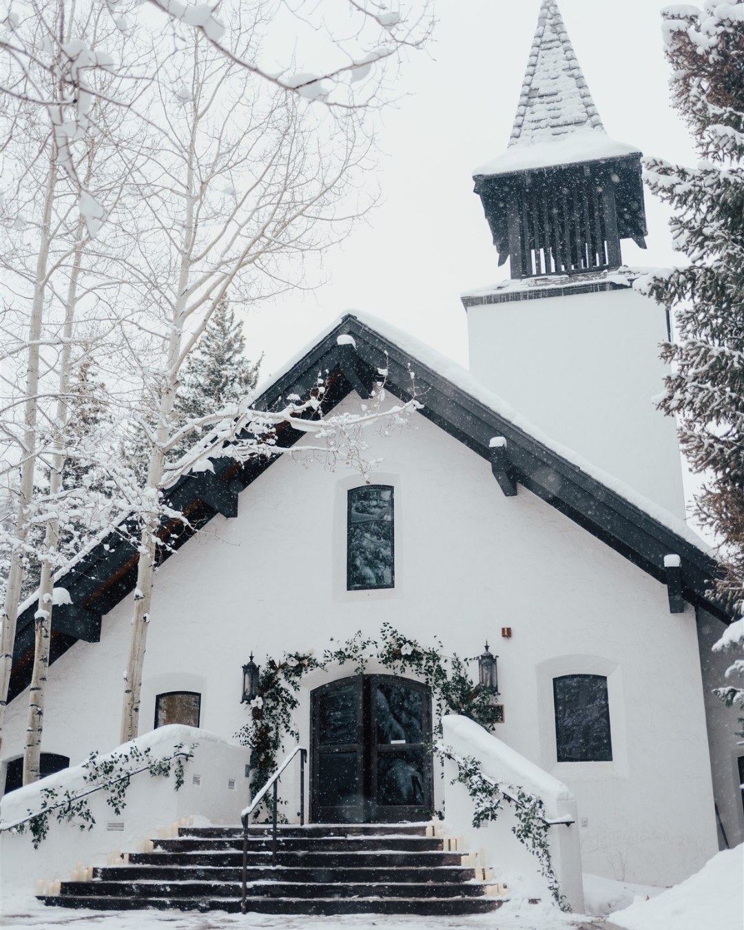 a white chapel with a steeple and trees in the snow 