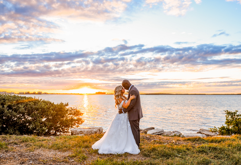 bride and groom pose at sunset by harbor
