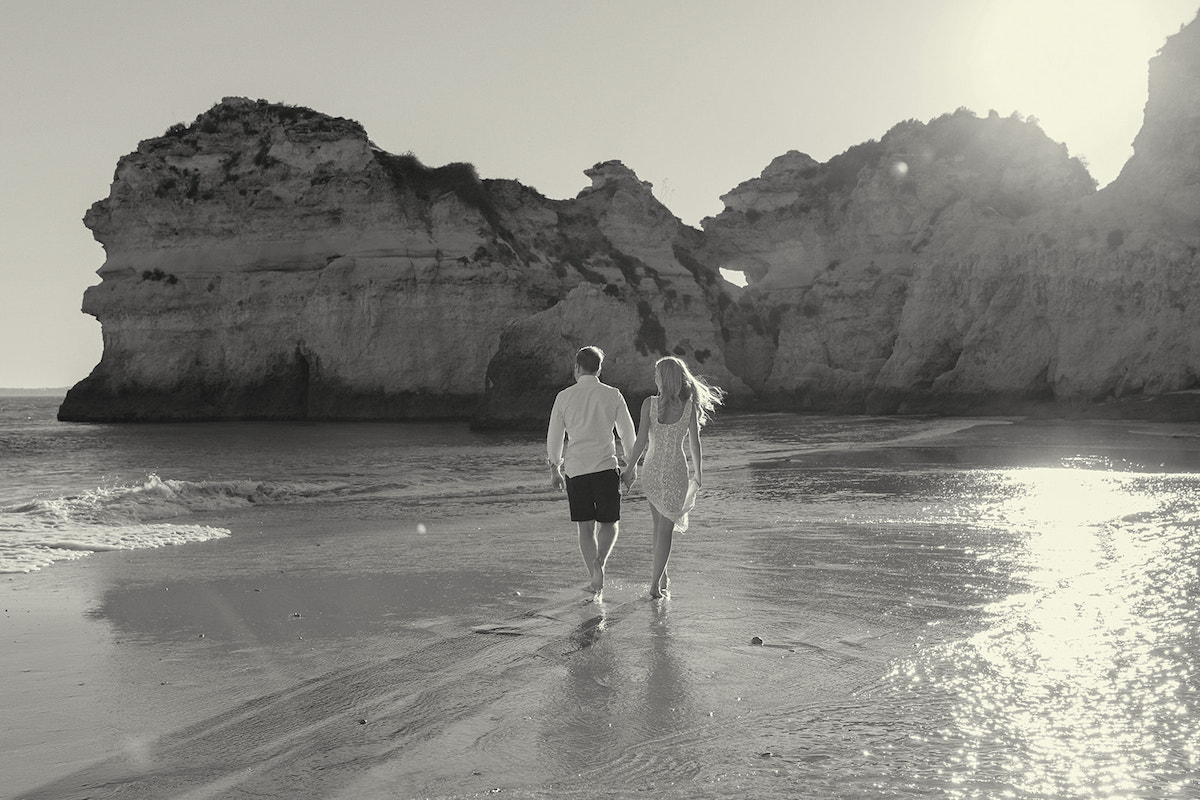 couple walking away on a beach in Portugal with a jetting rock formation in the background