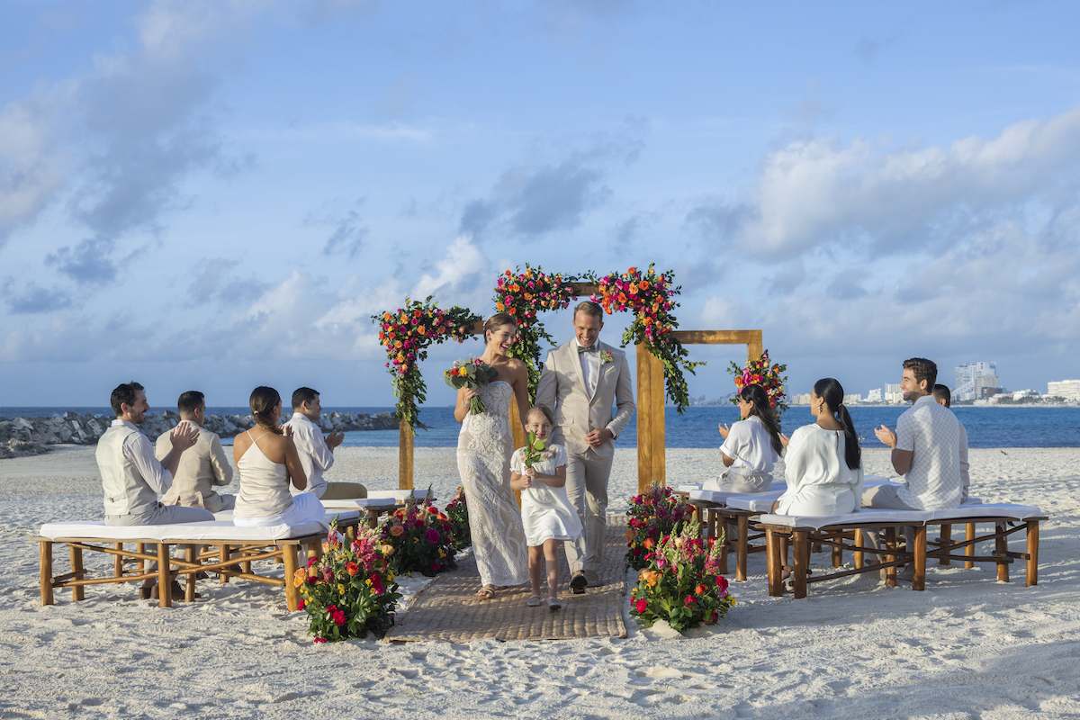 wedding ceremony with three wooden arches on beach as couple walk down aisle