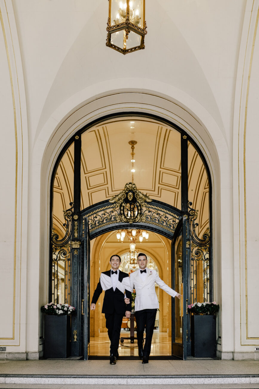 two grooms walking out front arched entrance