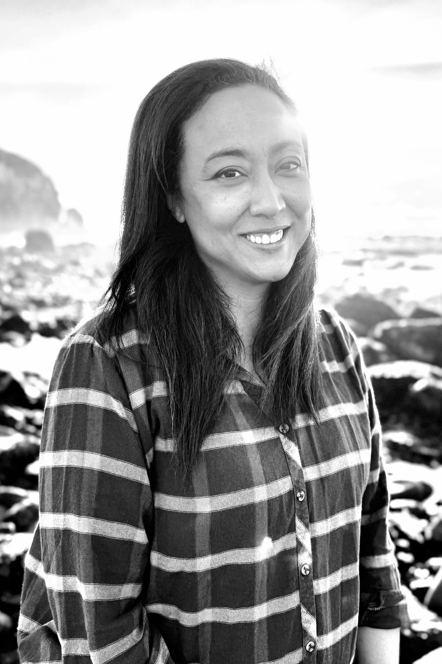 woman with dark hair smiling on rocky beach