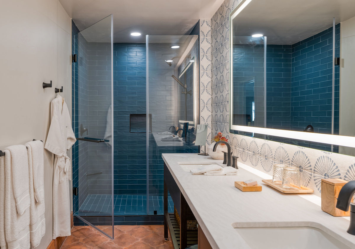 Modern bathroom with blue tiles, glass shower cubicle, and a patterned accent wall. towels hang neatly beside the sink area with terracotta flooring.