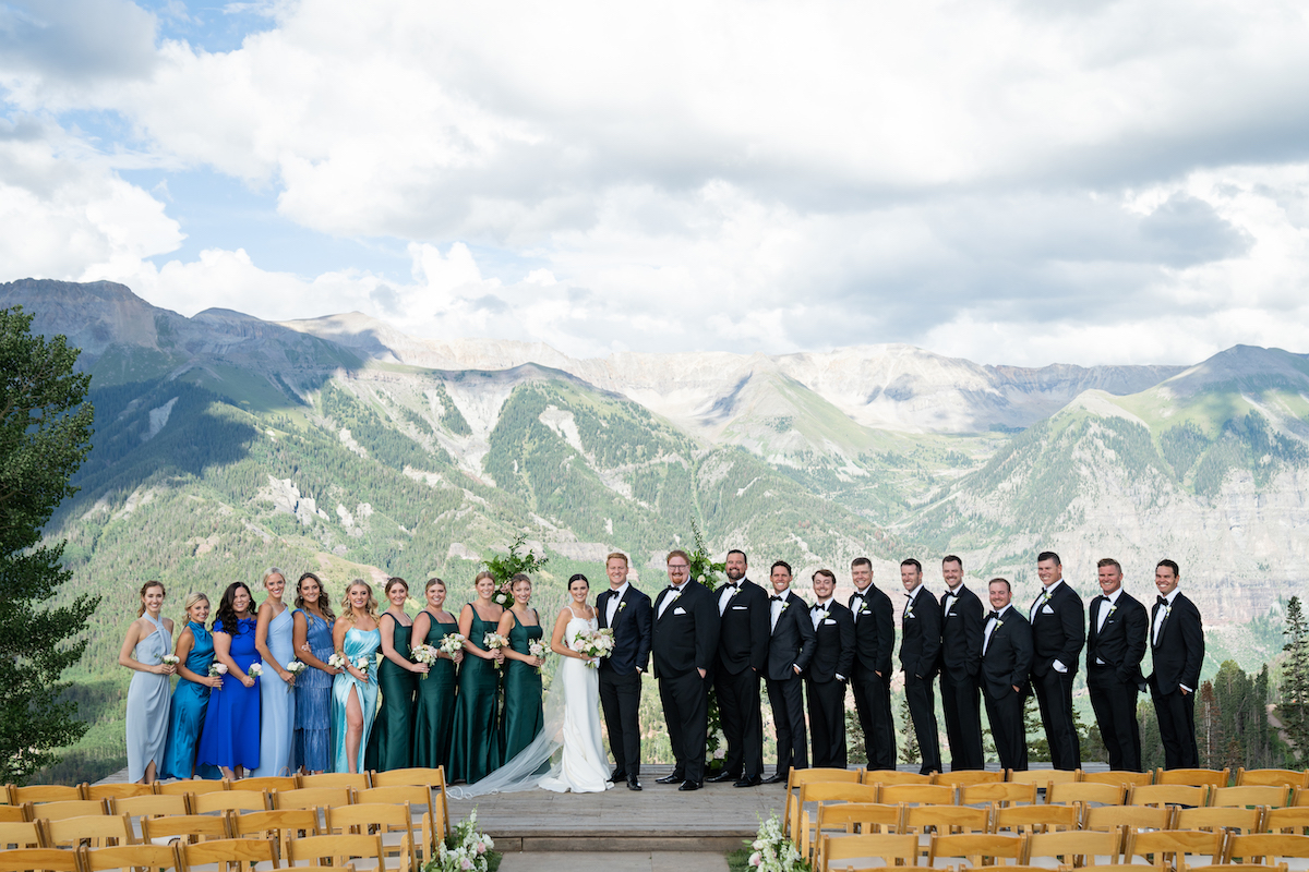 wedding party in blue and black pose in front of Aspen mountain range in summer