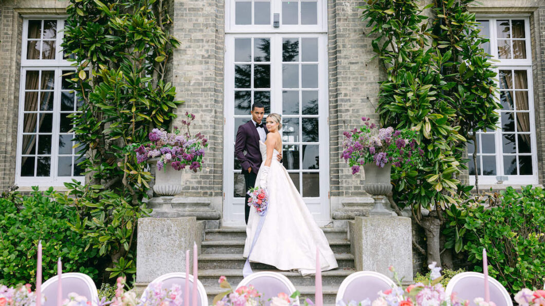 bride and groom pose on steps near window with table in foreground