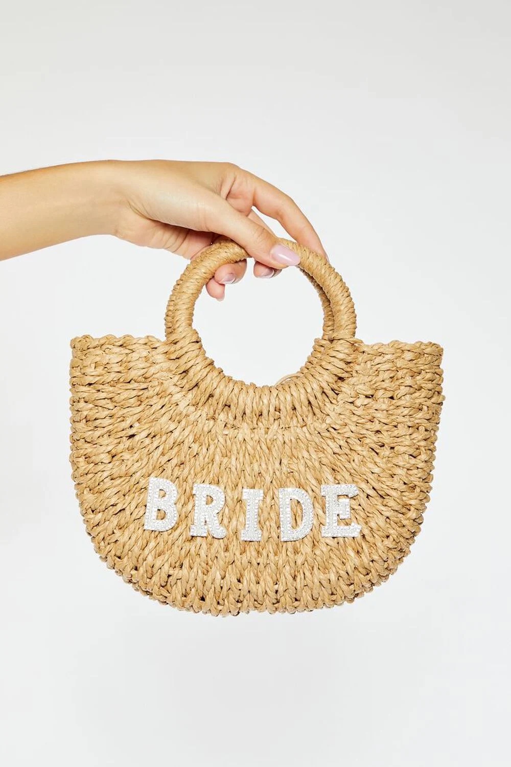 A hand holds a woven handbag with round handles from Forever 21. The word BRIDE is displayed in white letters on the front of the Bride Basketwoven Tote Bag.
