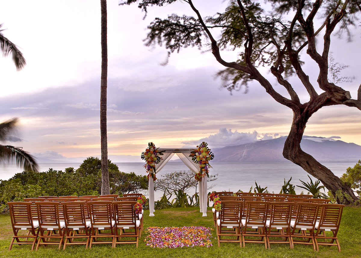 wedding ceremony setup with tropical florals on wooden arch at sunset