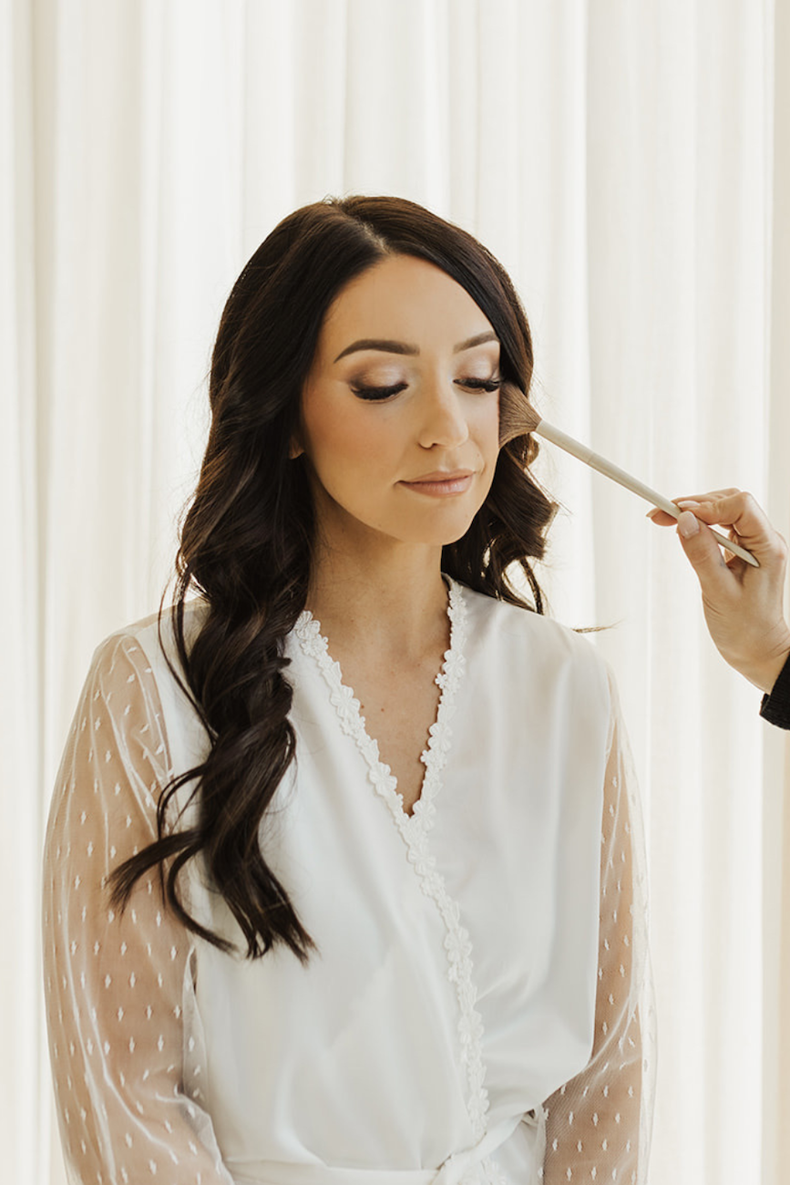 woman in white robe with lace getting makeup done