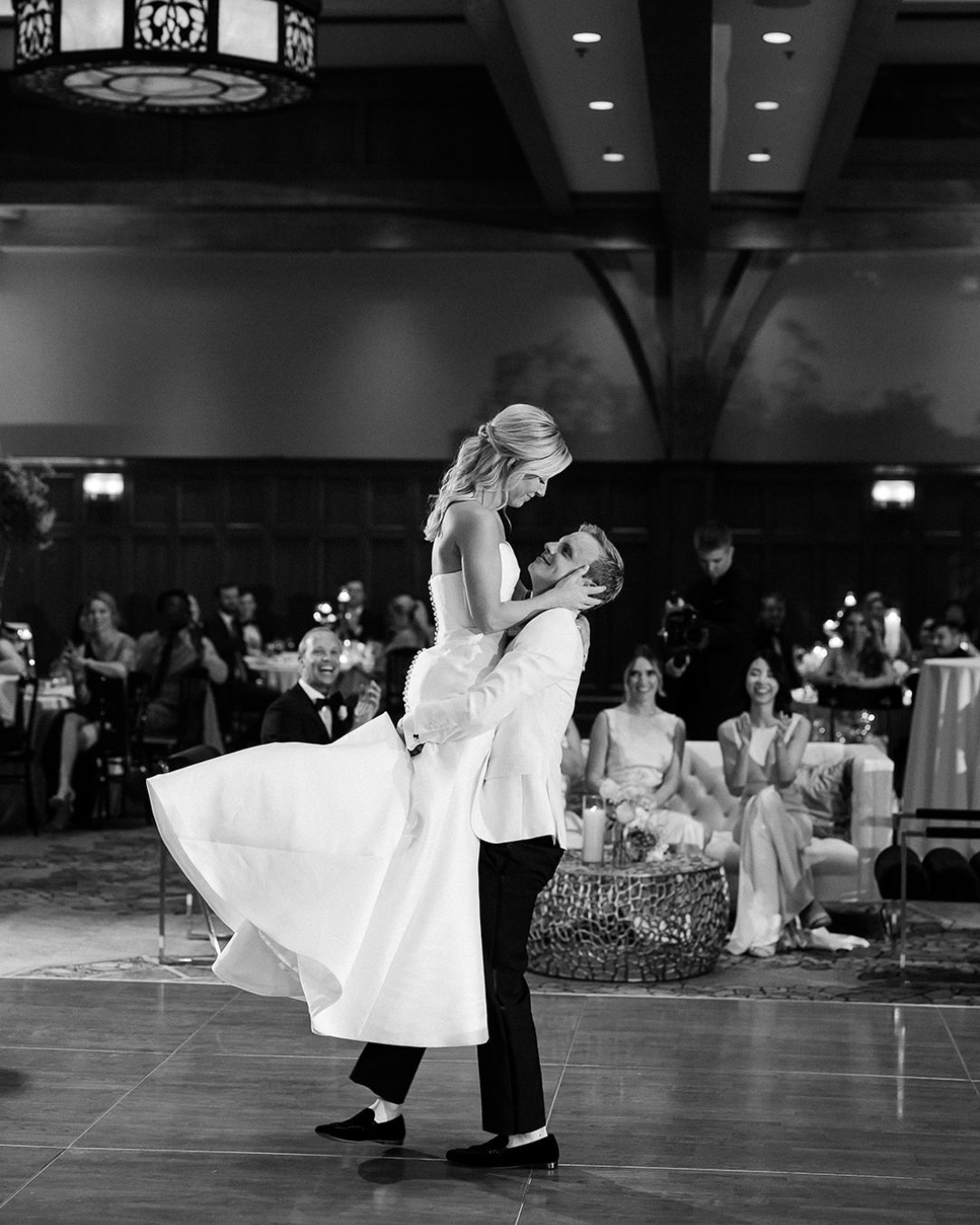groom lifts his bride up by waist as they dance at their wedding reception