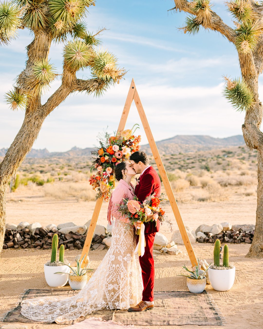 couple kiss under A frame altar, framed by Joshua trees and potted cactus