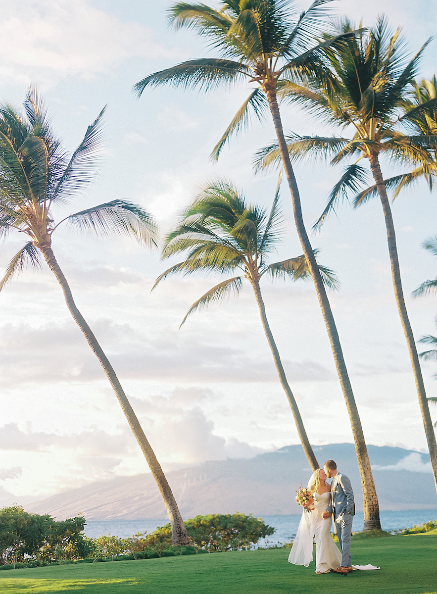 couple walk hand in hand on lawn near beach with palm trees swaying in the breeze