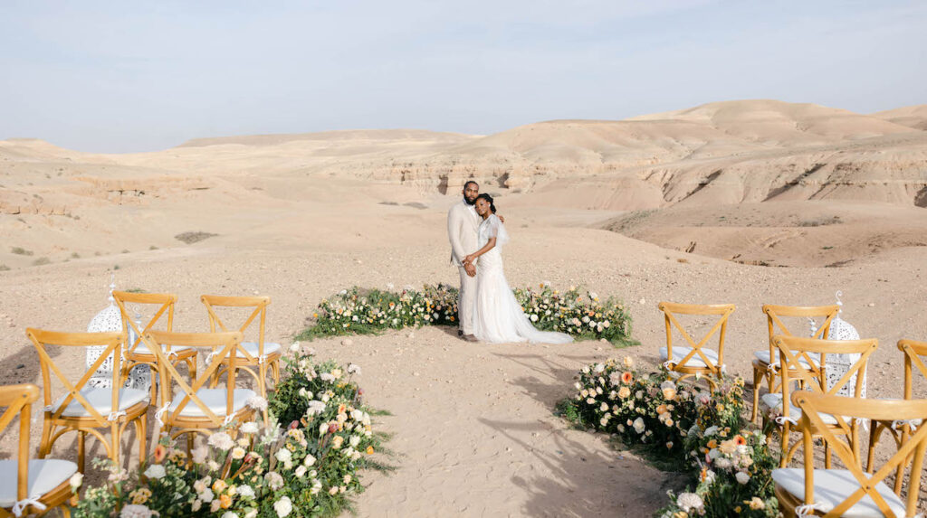 a couple embraces at the altar surrounded by a semi circle of white and pink florals with desert mountains in the background