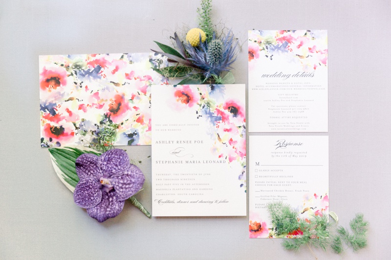 Floral-themed wedding invitation suite with envelopes, RSVP card, and decorative flowers arranged on a light surface.