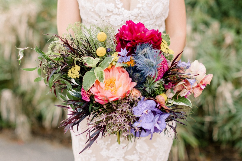 A person in a white lace dress holds a large, colorful bouquet of assorted flowers and greenery.