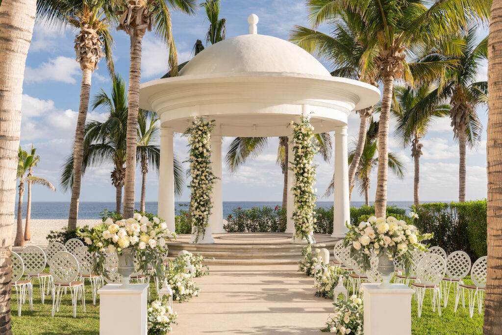 gazebo set up for a wedding with the aisle lined in white roses and a beach and ocean backdrop